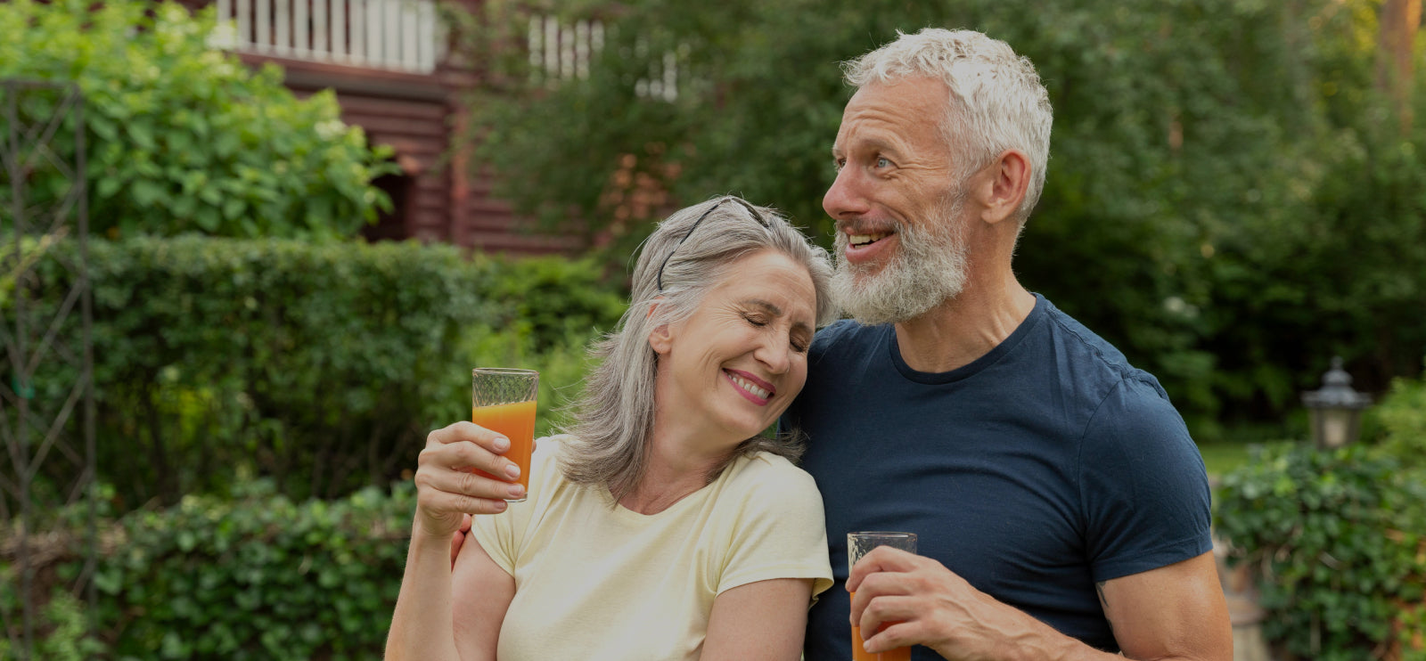 Man and woman sitting together outdoors, holding drinks, with a garden background.